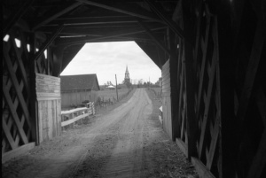 View of the inside of a Covered Bridge with a Bell-Tower in the distance 