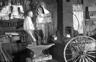 A blacksmith in Saint-Fidèle, Quebec, crafting an iron tyre (rim) for a carriage wheel